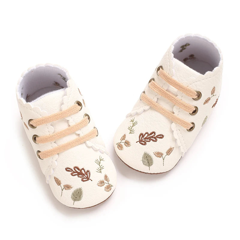 Top-down view of white scalloped baby girl crib shoes.