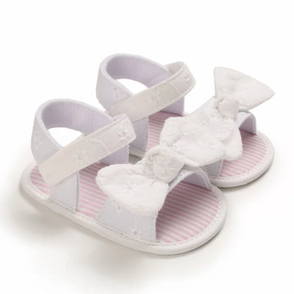 Pair of white baby girl soft sole sandals with an oversized eyelet lace bow and striped insole.