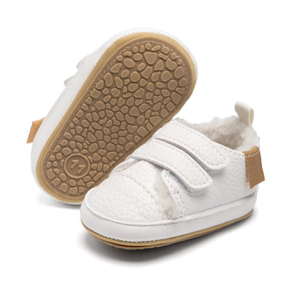 One white infant sneaker standing upright next to another showing the flexible, textured anti-slip rubber sole.