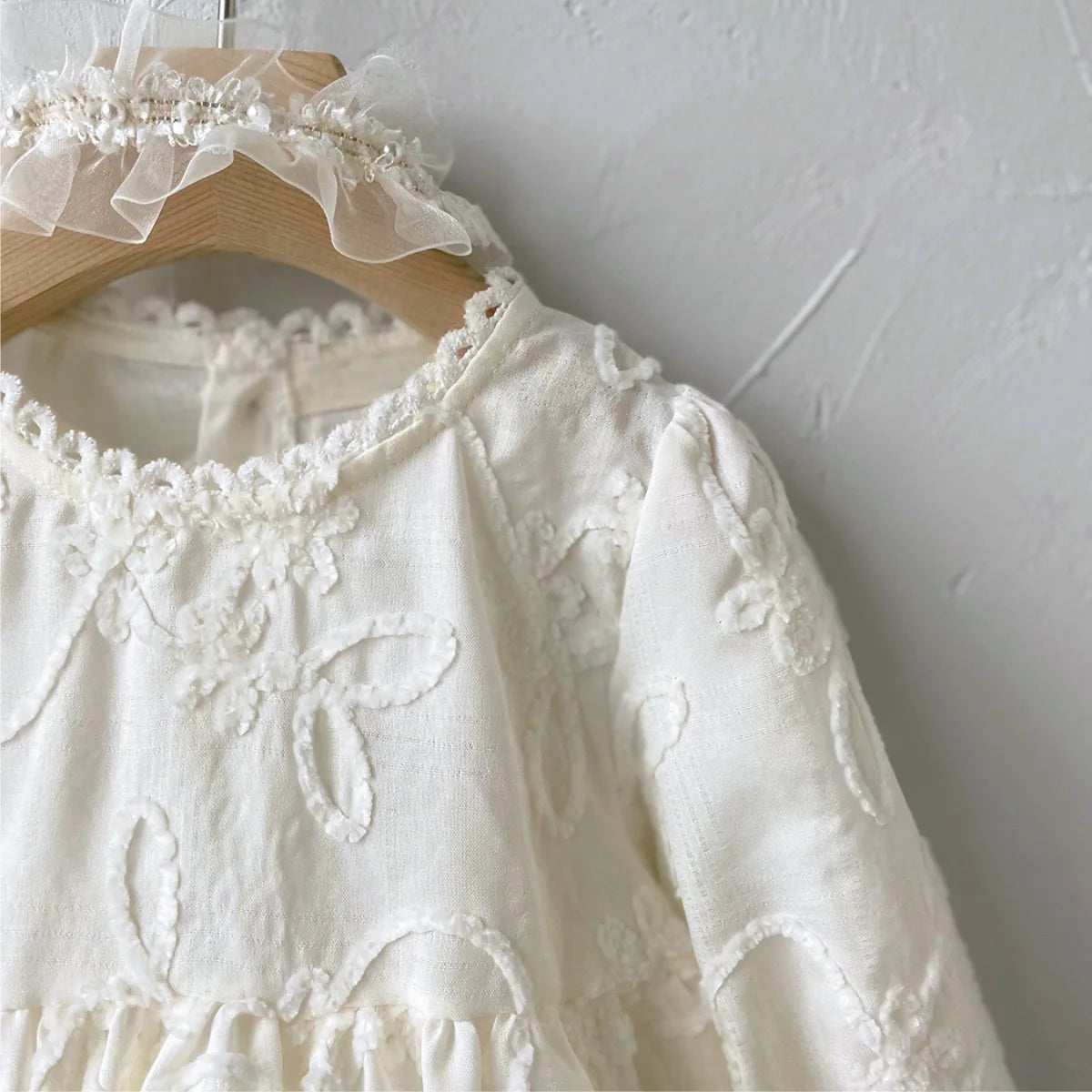 Close-up of the delicate white floral embroidery and scalloped neckline detail on the long sleeve dress.