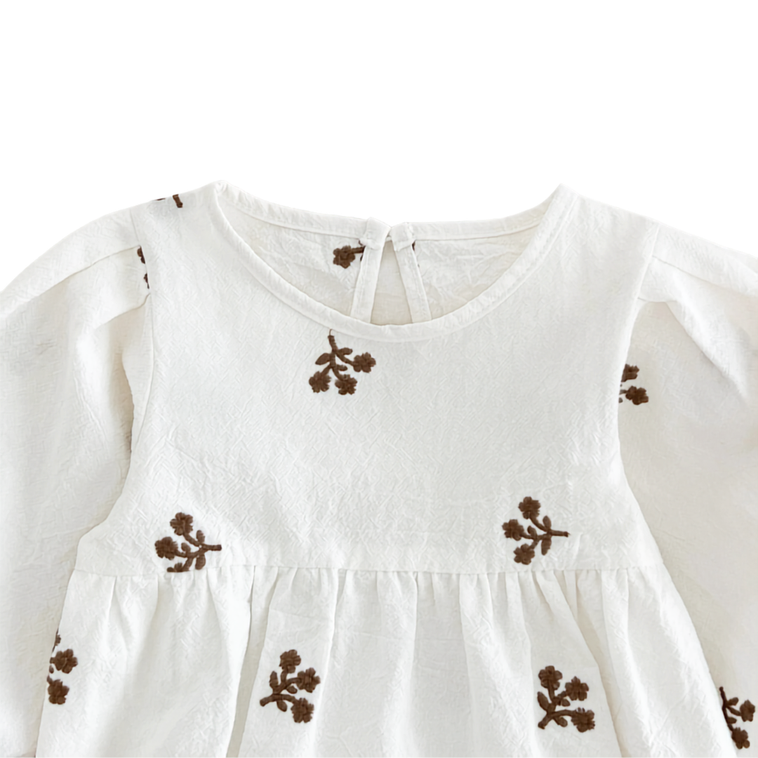 Close-up of the chest area on the white baby romper showing the gathered waistline and brown embroidery details.