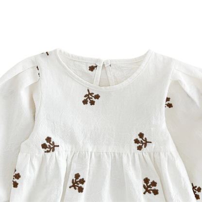 Close-up of the chest area on the white baby romper showing the gathered waistline and brown embroidery details.