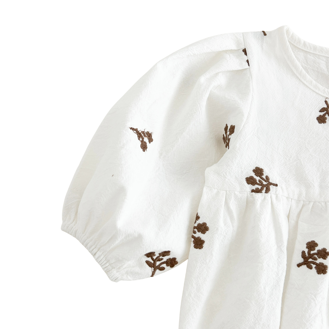 Close-up of the left shoulder and gathered sleeve on the white floral embroidered baby romper.