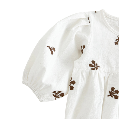Close-up of the left shoulder and gathered sleeve on the white floral embroidered baby romper.