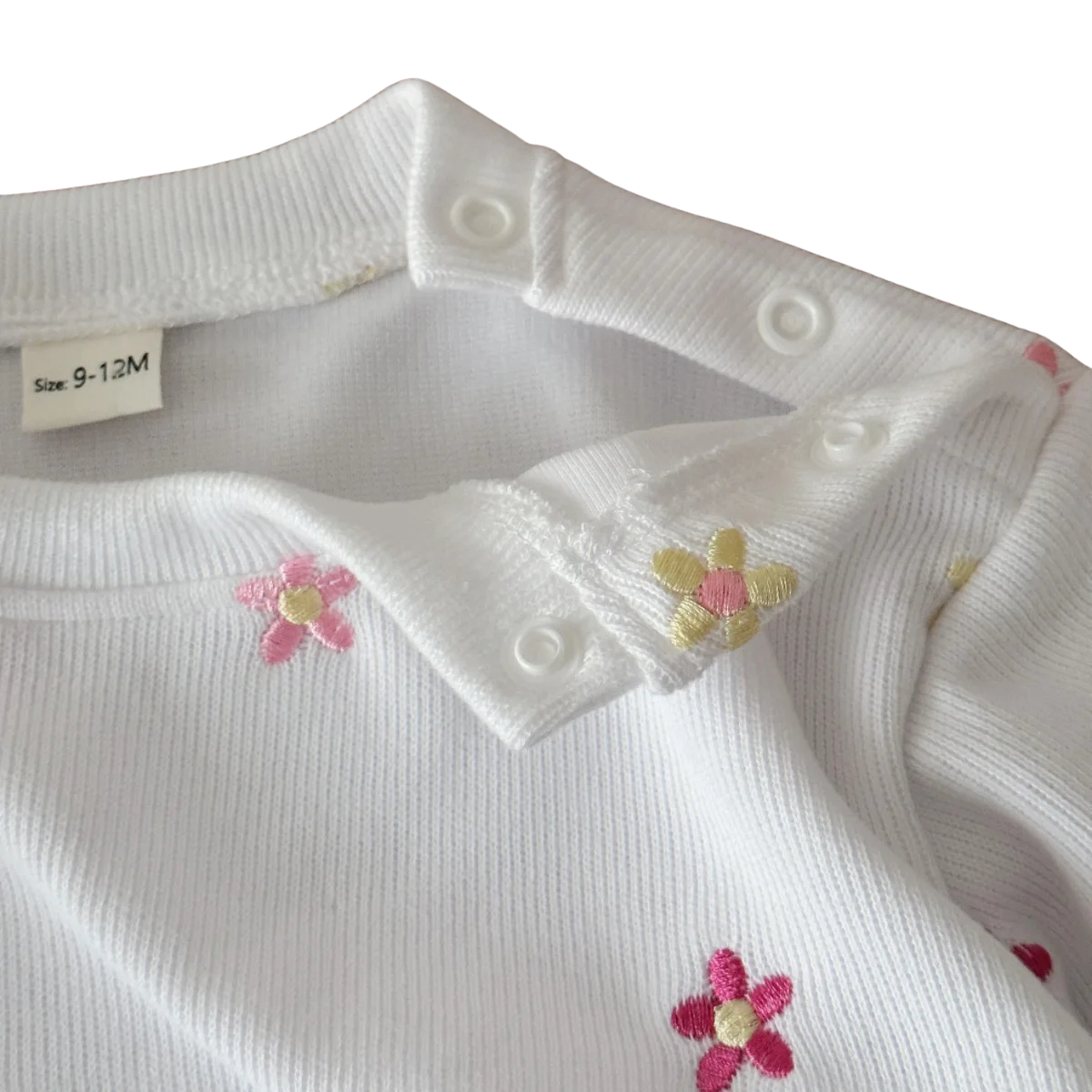 Close-up of the white baby sweatshirt showing the shoulder snaps unfastened for easy dressing, detailed with pink and yellow embroidered flowers.