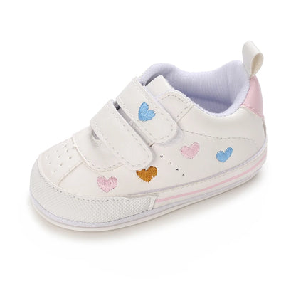 Side profile of a single white baby sneaker displaying pastel embroidered hearts, perforated toe details, and a pink heel tab.