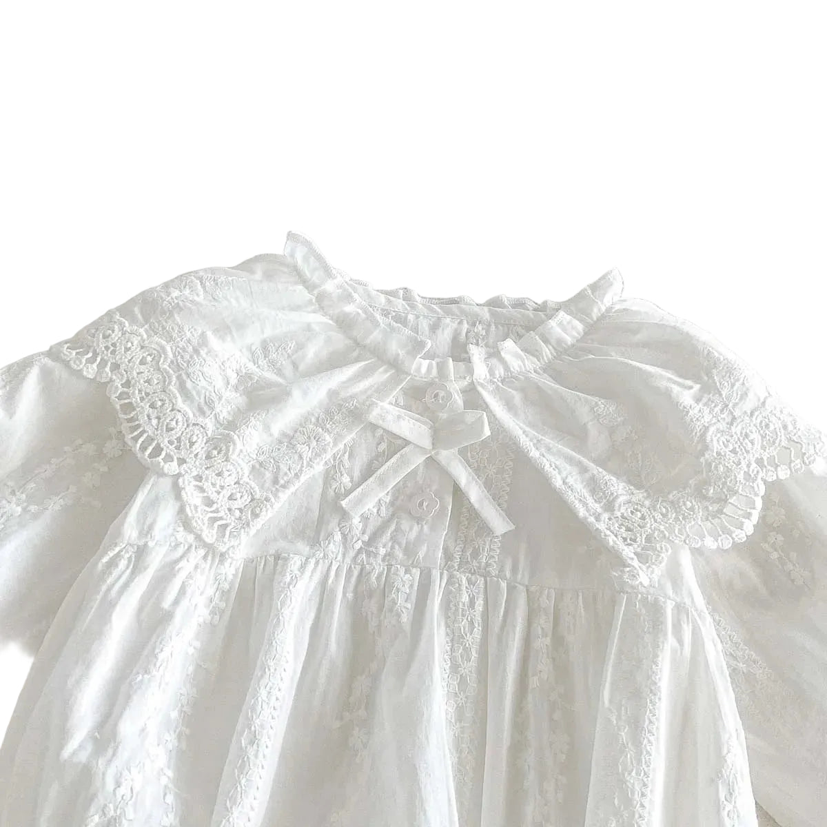 Close-up of the delicate scalloped lace Peter Pan collar and small ribbon bow on a white baby romper.
