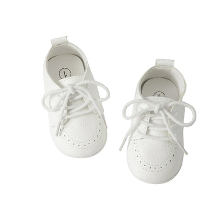 Overhead studio shot of a pair of Kidsely white textured pebbled faux leather baby brogue shoes with white laces.