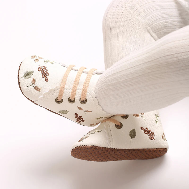 Baby wearing white embroidered soft sole pre-walker booties.