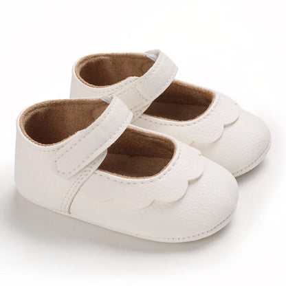 Infant girl's white Mary Jane shoes featuring a classic scalloped edge design, adjustable hook-and-loop strap, and a textured non-slip rubber sole for first walkers.