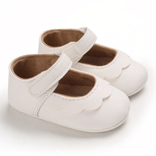 Infant girl's white Mary Jane shoes featuring a classic scalloped edge design, adjustable hook-and-loop strap, and a textured non-slip rubber sole for first walkers.