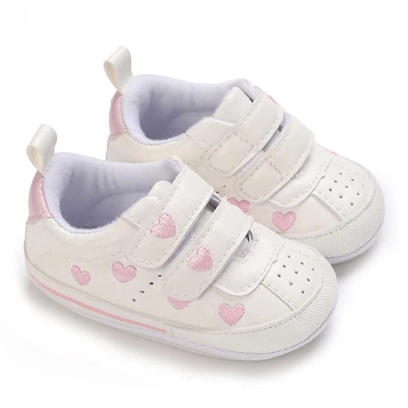 Angled pair of white first walker sneakers decorated with blue, pink, and gold hearts for baby girls.