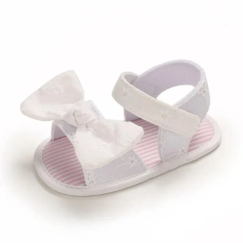 Single white baby girl soft sole sandal featuring an eyelet lace bow and ankle strap.