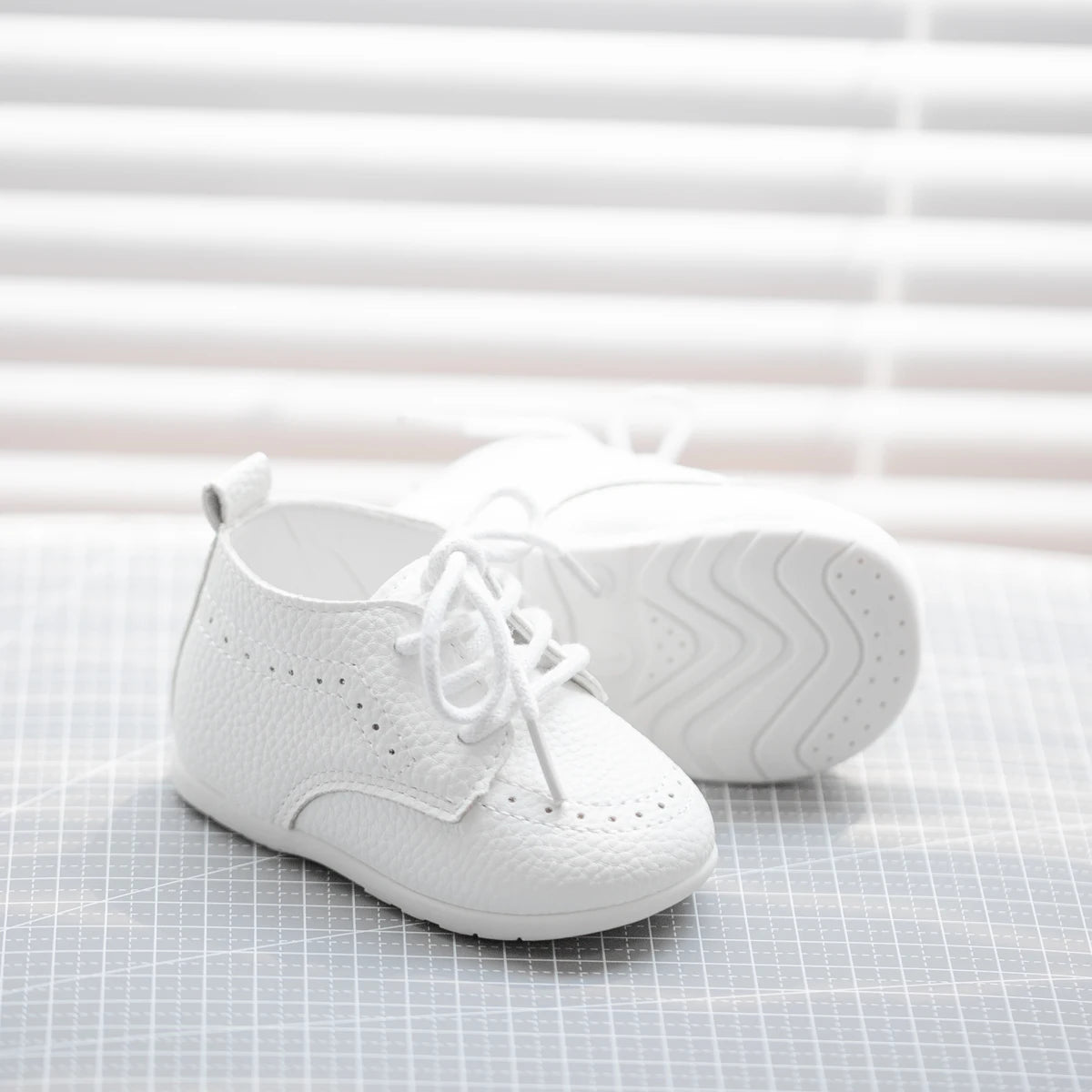 Single white textured pebbled baby shoe showing the intricate side stitching and traditional brogue perforations.