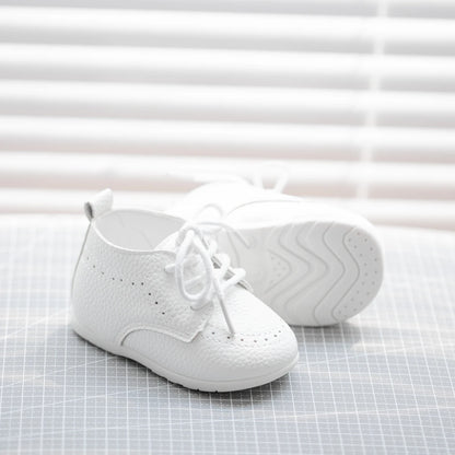 Single white textured pebbled baby shoe showing the intricate side stitching and traditional brogue perforations.