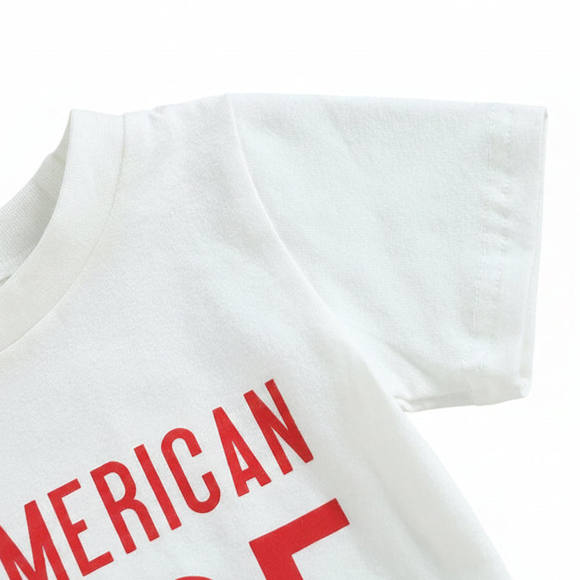 Close-up detail of the red "All American Dude" typography on the white toddler graphic tee.