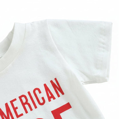 Close-up detail of the red "All American Dude" typography on the white toddler graphic tee.