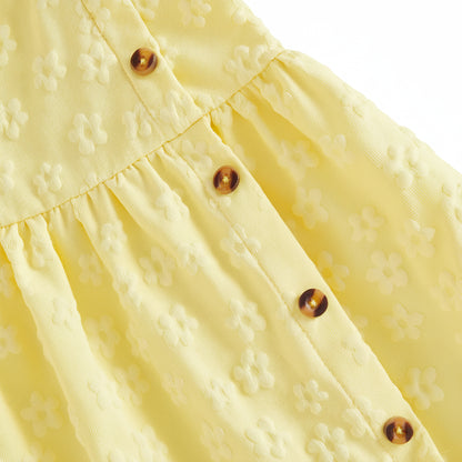 Close-up macro shot of the 3D floral embossed pattern on the soft yellow baby dress fabric, highlighting the faux-wood side buttons and pleated waist details.