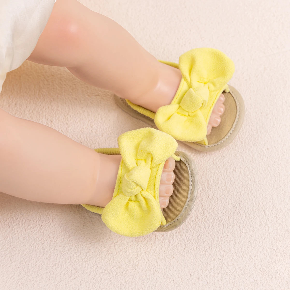 Baby wearing soft yellow summer sandals with brushed fabric bows, lying comfortably.