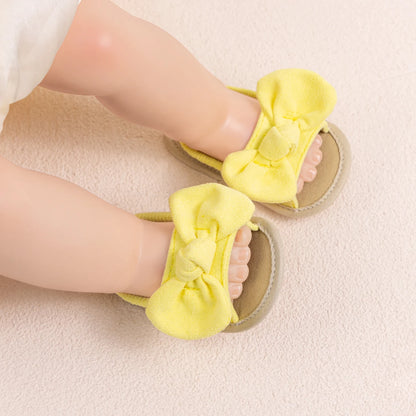 Baby wearing soft yellow summer sandals with brushed fabric bows, lying comfortably.