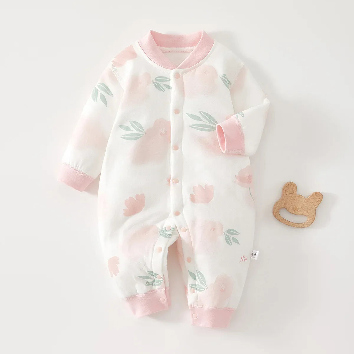 Soft cotton baby jumpsuit with watercolor pink floral design. Long sleeve coverall for infants with pink collar and cuffs, featuring easy-snap buttons.