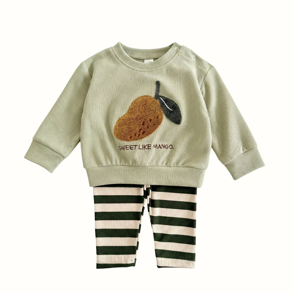 Mint green baby sweatshirt featuring a textured mango fruit patch and text "Sweet Like Mango," paired with dark green and cream striped pants.