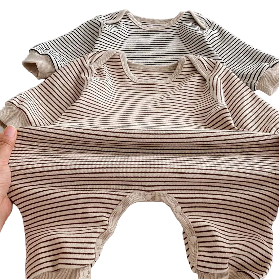 Hands pulling the Toasted Latte striped baby romper horizontally to demonstrate the stretchy 5% spandex cotton blend fabric.