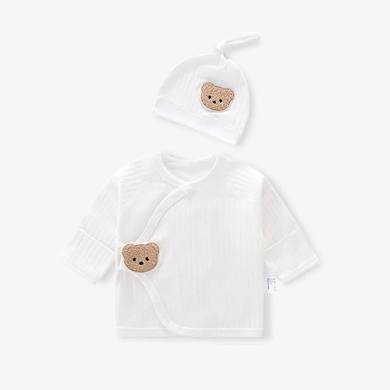 Flat lay of cream white newborn ribbed kimono top and matching knot hat featuring a textured teddy bear patch.