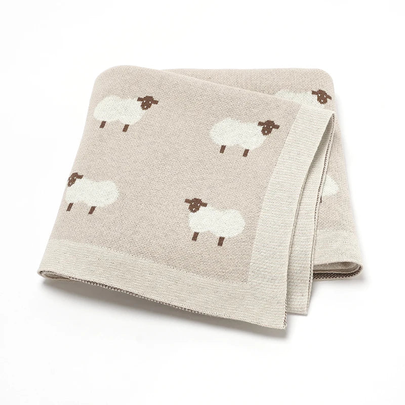 100% cotton knitted baby blanket in Oatmeal with a white lamb pattern, folded to show the soft, chunky knit texture.