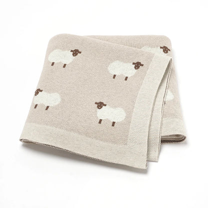 100% cotton knitted baby blanket in Oatmeal with a white lamb pattern, folded to show the soft, chunky knit texture.
