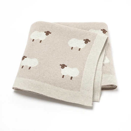 100% cotton knitted baby blanket in Oatmeal with a white lamb pattern, folded to show the soft, chunky knit texture.