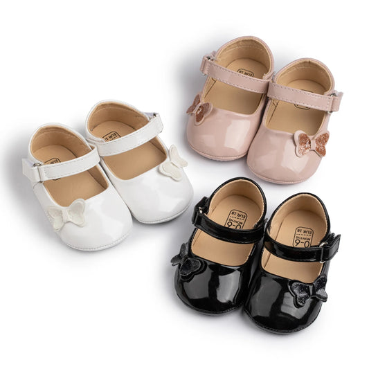 three pairs of glossy patent baby girl mary jane shoes in pink, white, and black with glitter butterfly bows and non-slip rubber soles