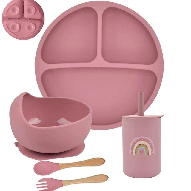 Pink silicone dinnerware set with plate, bowl, cup, and utensils on a white background