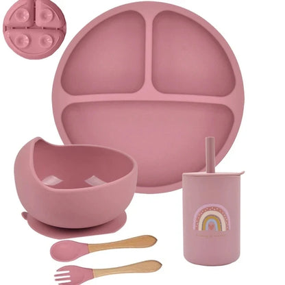 Pink silicone dinnerware set with plate, bowl, cup, and utensils on a white background