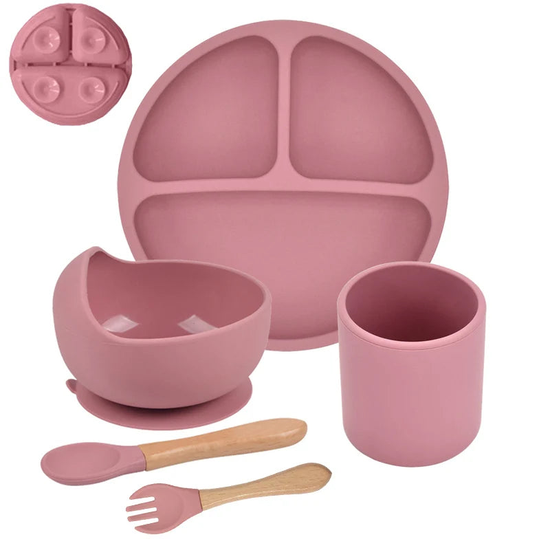 4-piece baby tableware set arranged flat, including a divided suction plate, silicone cup with straw, and wooden-handled spoon and fork.