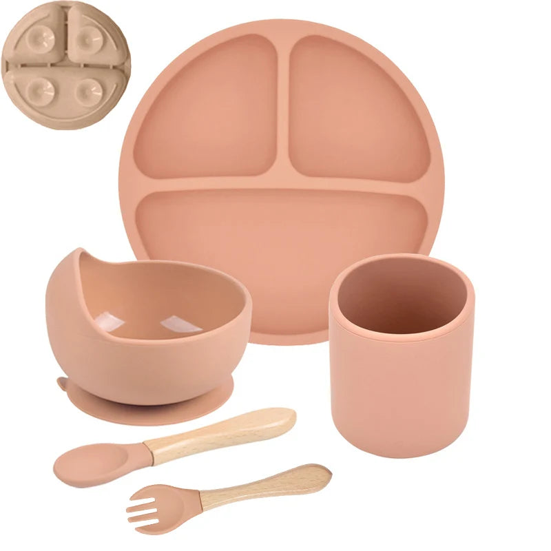 Orange children's silicone dinner set with plate, bowl, cup, spoon, and fork on a white background.