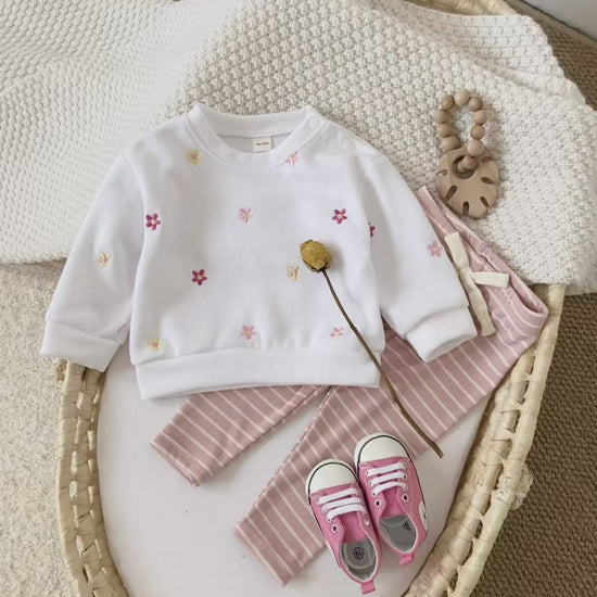 Video thumbnail showing a flat lay of the white floral sweatshirt and striped leggings set in a woven baby basket with pink shoes.