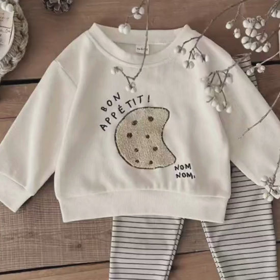A video thumbnail showing a flat lay of the cream cookie sweatshirt and striped leggings on a rustic wooden floor.