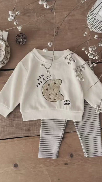 A video thumbnail showing a flat lay of the cream cookie sweatshirt and striped leggings on a rustic wooden floor.