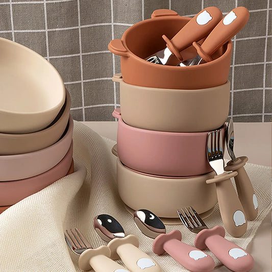 Set of children's cutlery and bowls in pastel colors on a neutral background