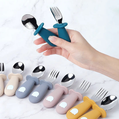 Hand holding a blue children's fork and spoon set with more sets displayed on a marble surface.