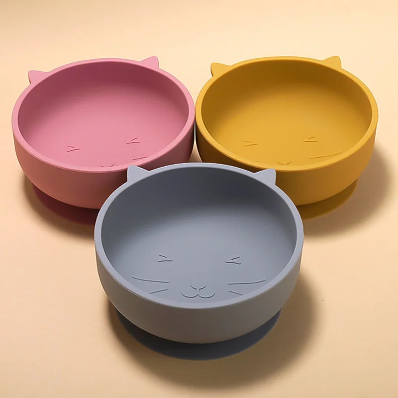 Three colorful silicone bowls with cat ear designs on a beige background