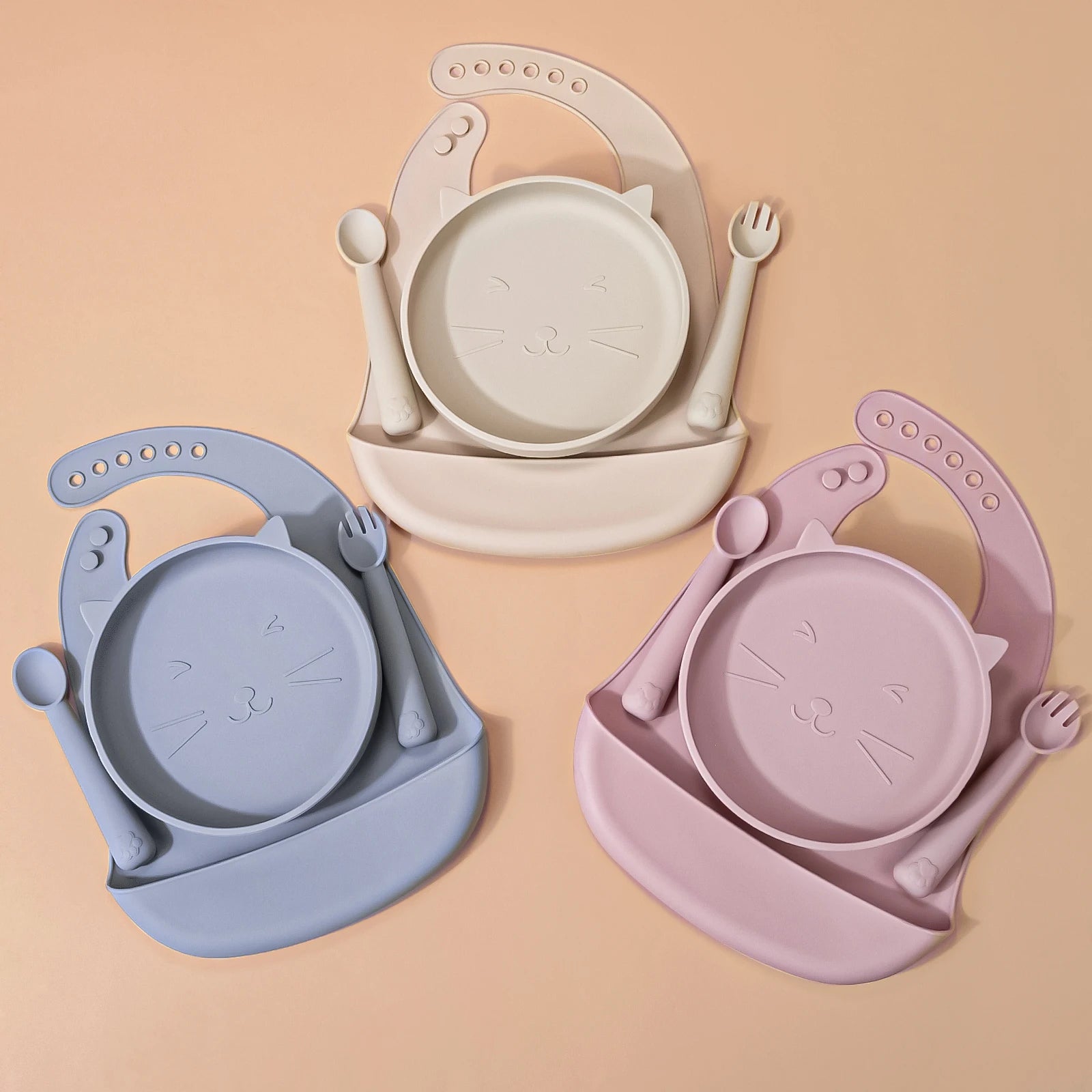 4-piece silicone feeding set including a rectangular divided suction tray, bib with pocket, and matching fork and spoon.