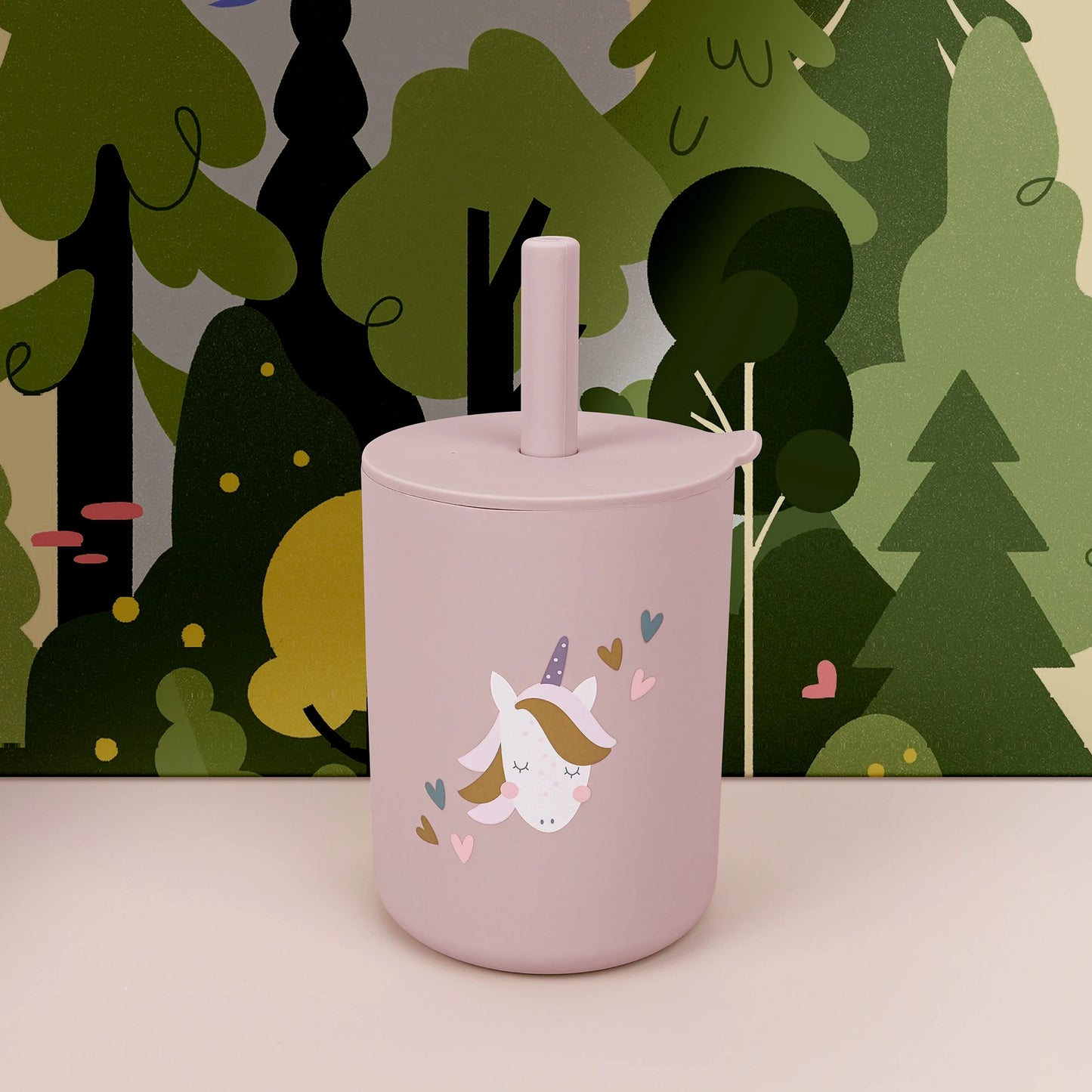 Pink tumbler with a unicorn design against a forest background