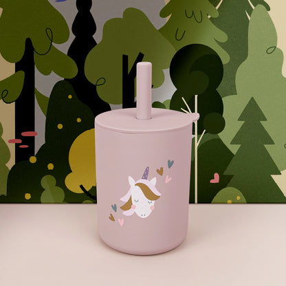 Pink tumbler with a unicorn design against a forest background