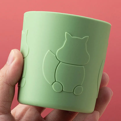 Green silicone cup with squirrel design held by a hand against a red background