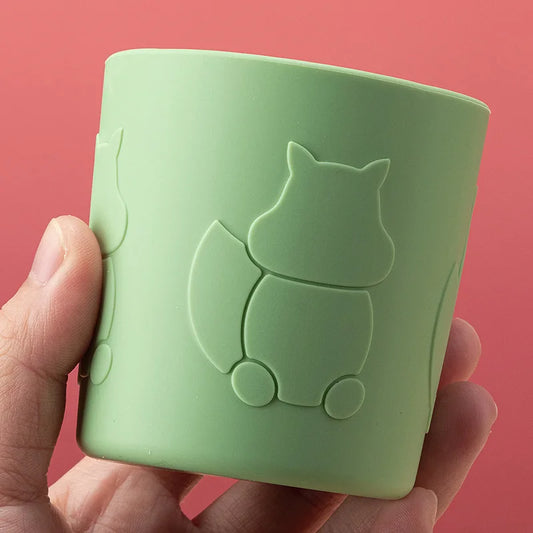 Green silicone cup with squirrel design held by a hand against a red background