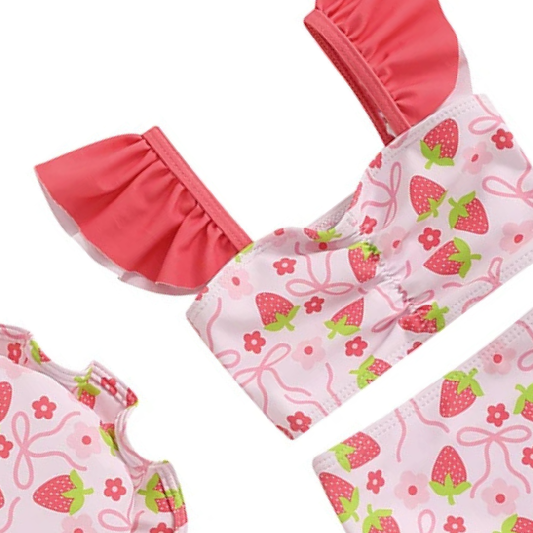 Close-up detail of the pink strawberry print fabric and ruffle flying sleeves on a baby girl's swimsuit showing the high-quality stitching.