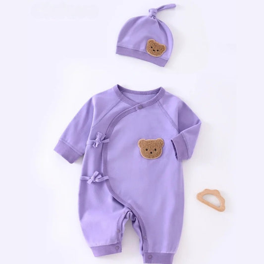 Flat lay of purple long sleeve baby kimono romper with side ties and matching knotted hat featuring teddy bear patches.