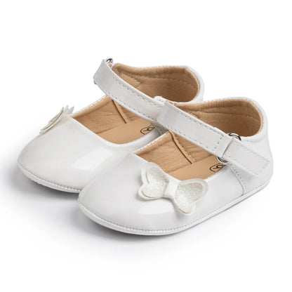 classic white patent baby girl crib shoes with shiny butterfly-knot accent and soft flexible bottoms.